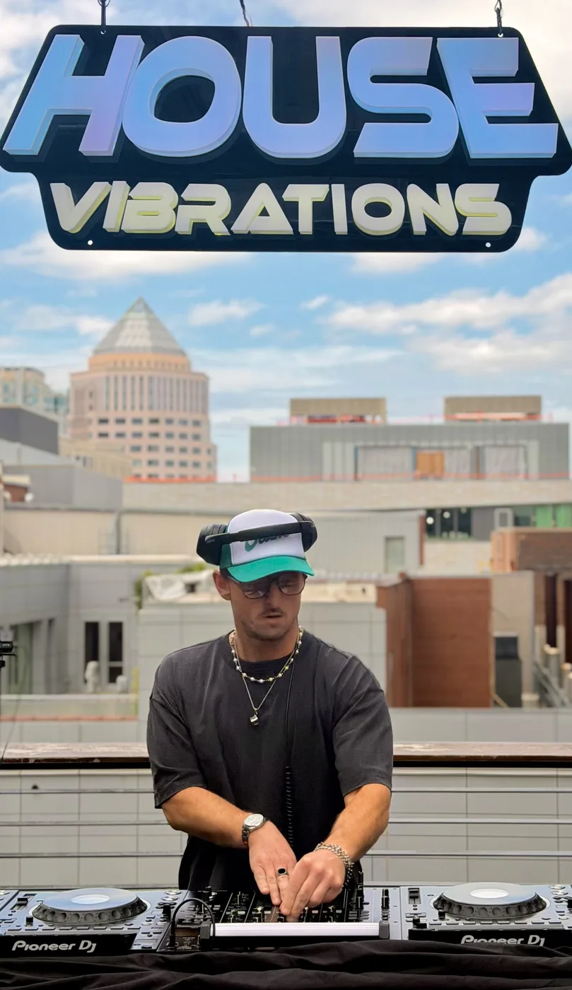 AUSTAL DJing on a rooftop under the House Vibrations sign, city skyline behind